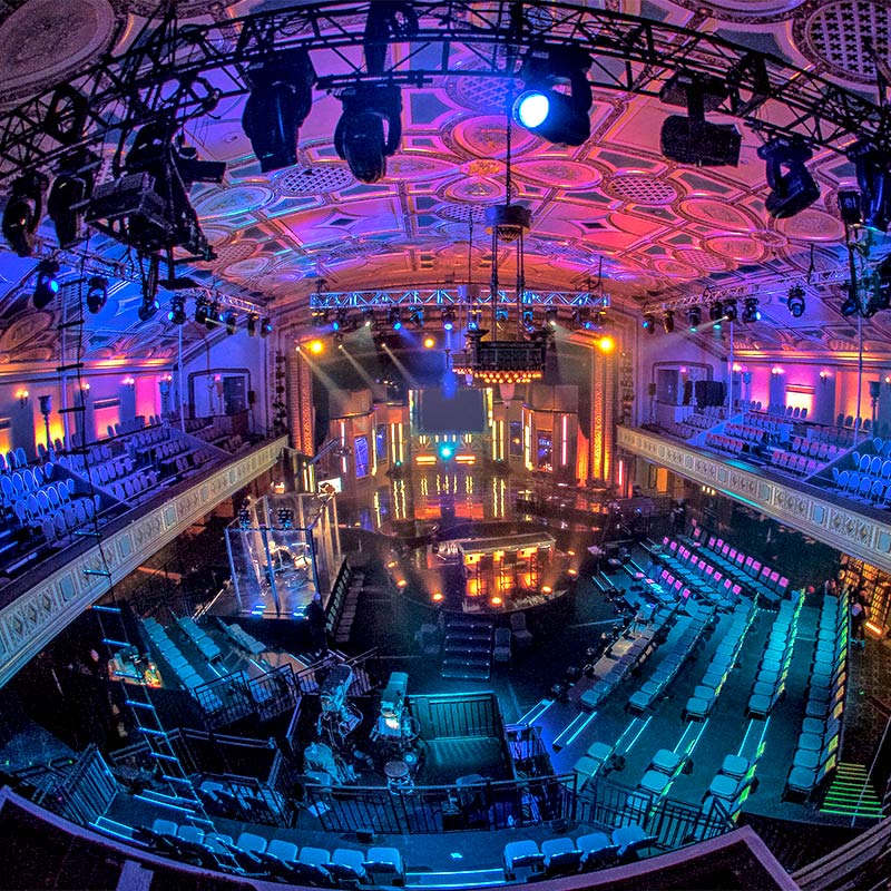 An expansive auditorium with a prominent stage illuminated by lights, offering ample seating for an audience.